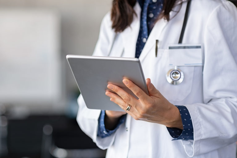 Close up of woman doctor hands using digital tablet at clinic. Closeup of doctor in labcoat and stethoscope holding digital tablet, reading patient report. Hands holding medical report, copy space.